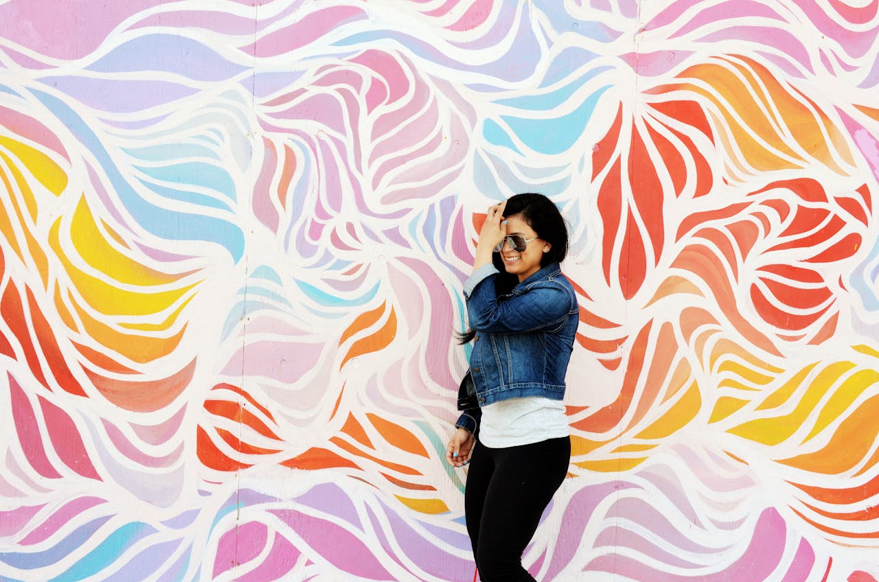A woman in a denim jacket poses joyfully against a vibrant mural in Asbury Park, NJ.
